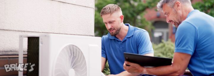 HVAC technicians inspecting and servicing an outdoor air conditioning unit with a tablet and tools.