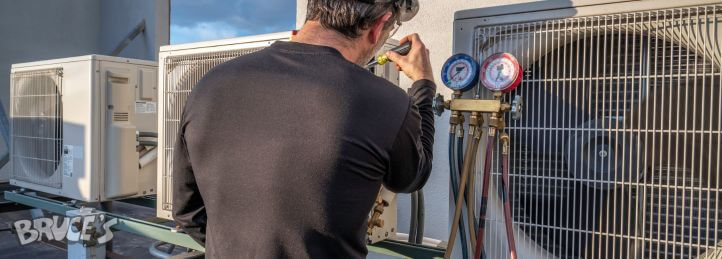 HVAC technician checking refrigerant levels with manifold gauges on a rooftop air conditioning unit.