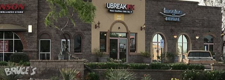 Storefront of a UBREAKIFIX electronics repair shop in a stone retail plaza with landscaped entrance.