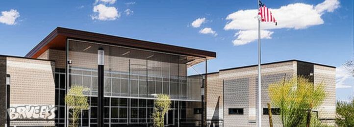 Modern civic building with glass facade and American flag flying in front under a blue sky.